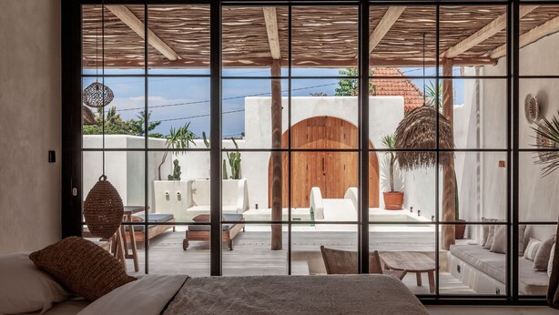 A modern bedroom with a large bed, a view through a sliding glass door to an outdoor patio with seating and plants. - Yucca Villas (Canggu)