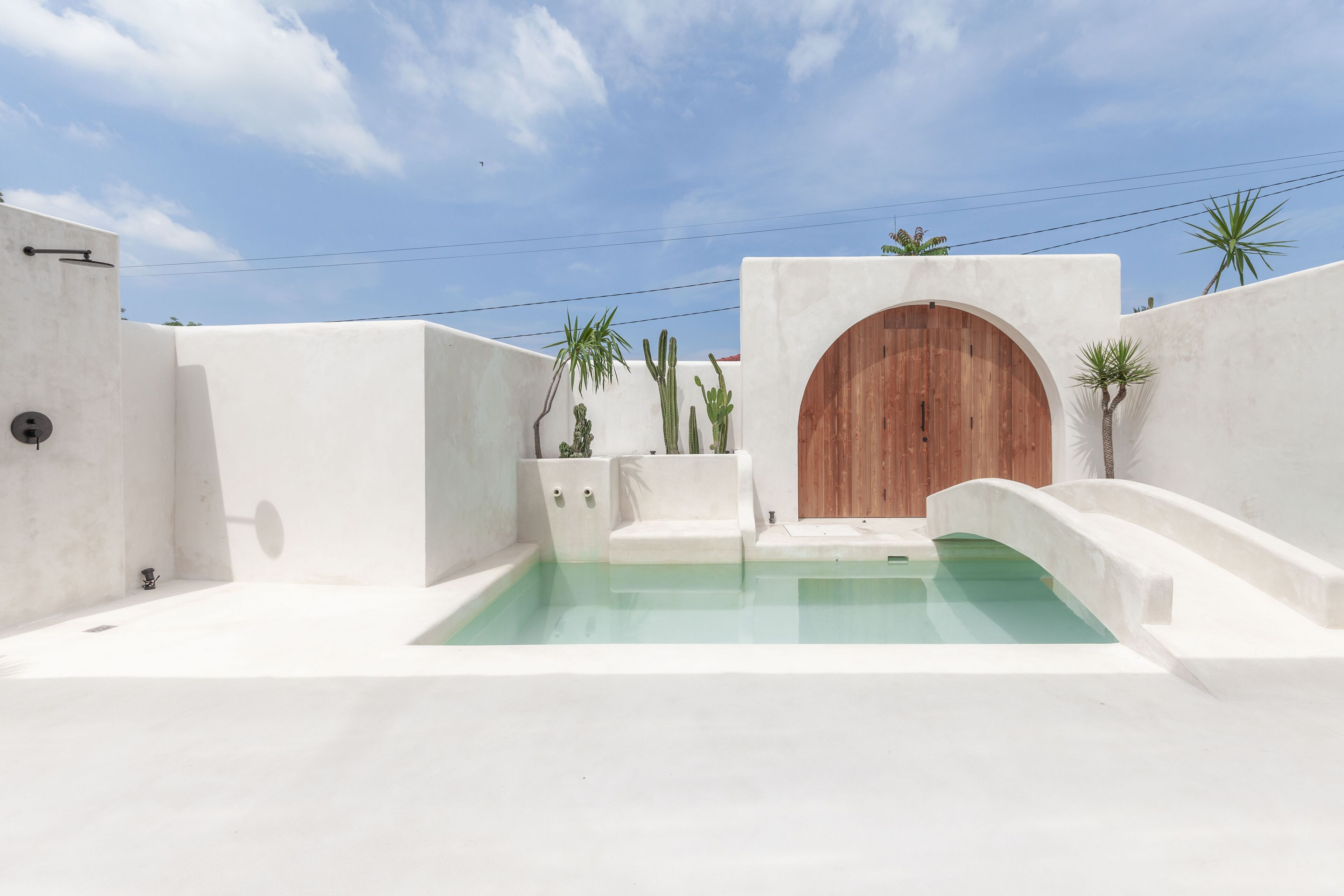 Un'area piscina esterna moderna con porta in legno, pareti bianche e design minimalista.