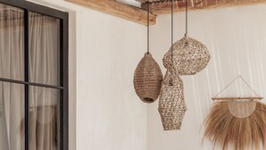 A cozy room with a large window, a wooden sofa, a small table, and hanging woven light fixtures. - Yucca Villas (Canggu)