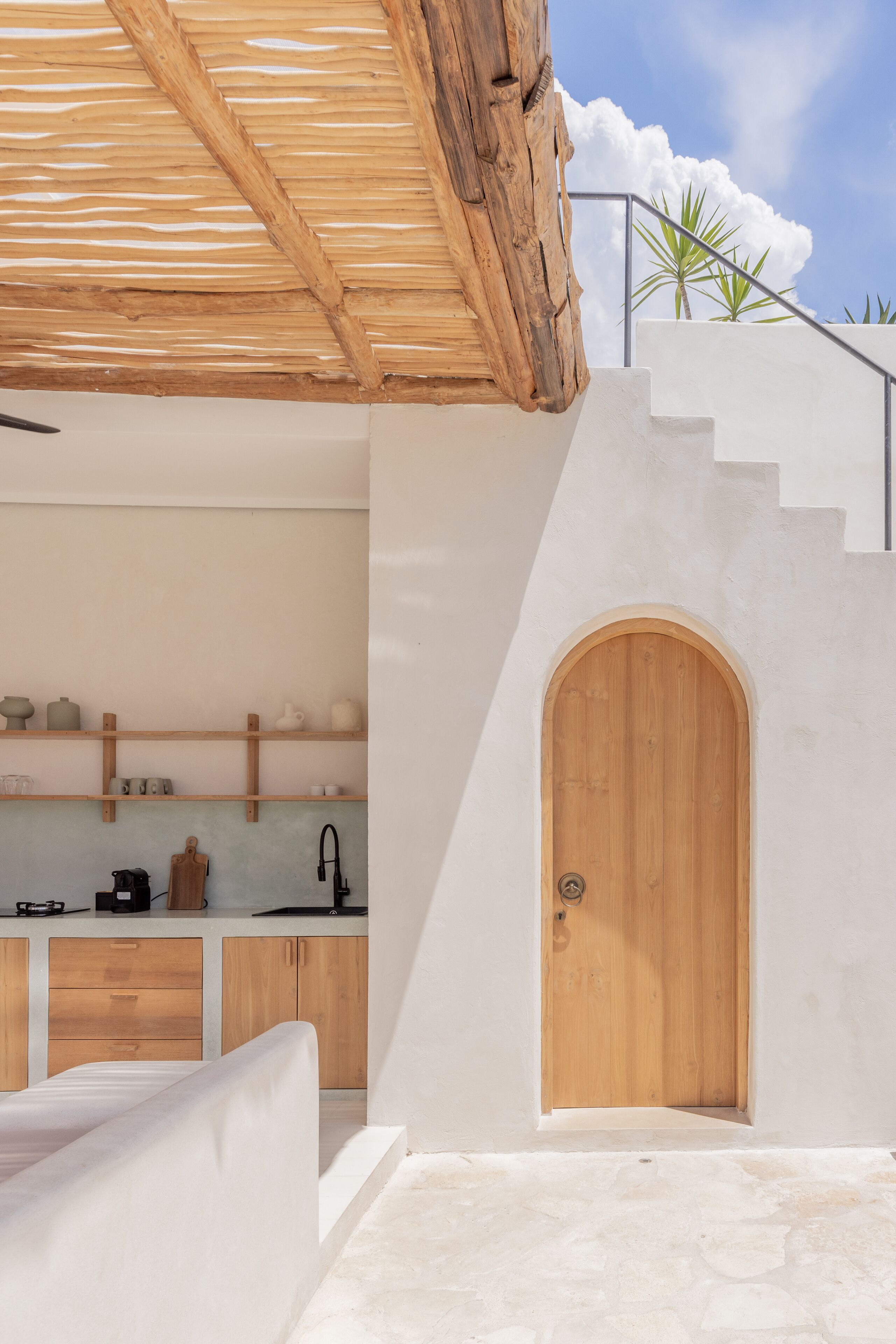 A modern kitchen with white cabinets, a wooden door, and a stone floor.