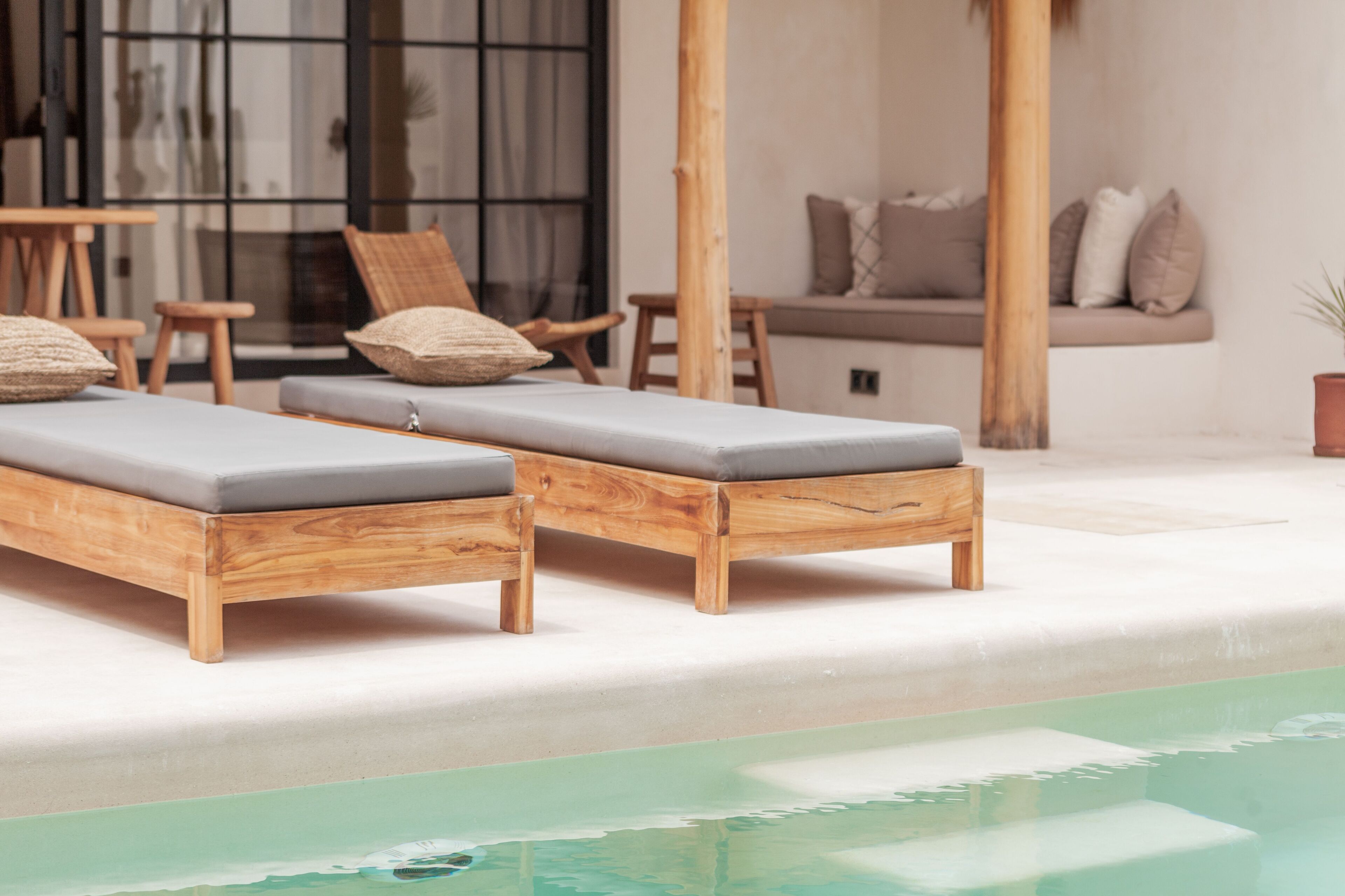 Un espace aménagé au bord de la piscine, avec des chaises longues en bois et un coin salon doté de coussins.