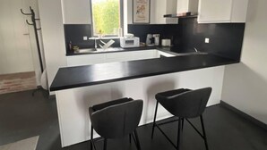 Una cocina moderna con encimera negra, armarios blancos y dos taburetes negros.