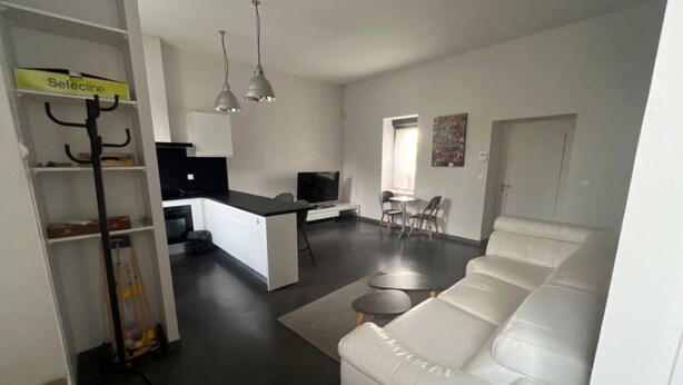 Una sala de estar moderna con un sofá blanco, una zona de comedor con mesa y sillas, y un área de cocina con televisor y cafetera.