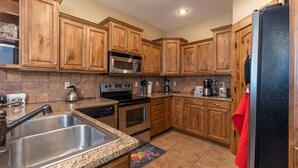 Eine Küche mit Holzausstattung, Edelstahlgeräten, Granitarbeitsplatten und einem schwarzen Kühlschrank.