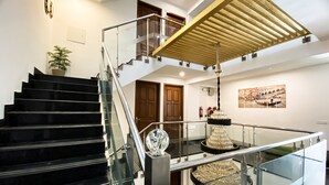 A modern interior with a black staircase, glass railings, a chandelier, and a wooden ceiling structure. - Sky Suites Huda City Center (Gurugram)