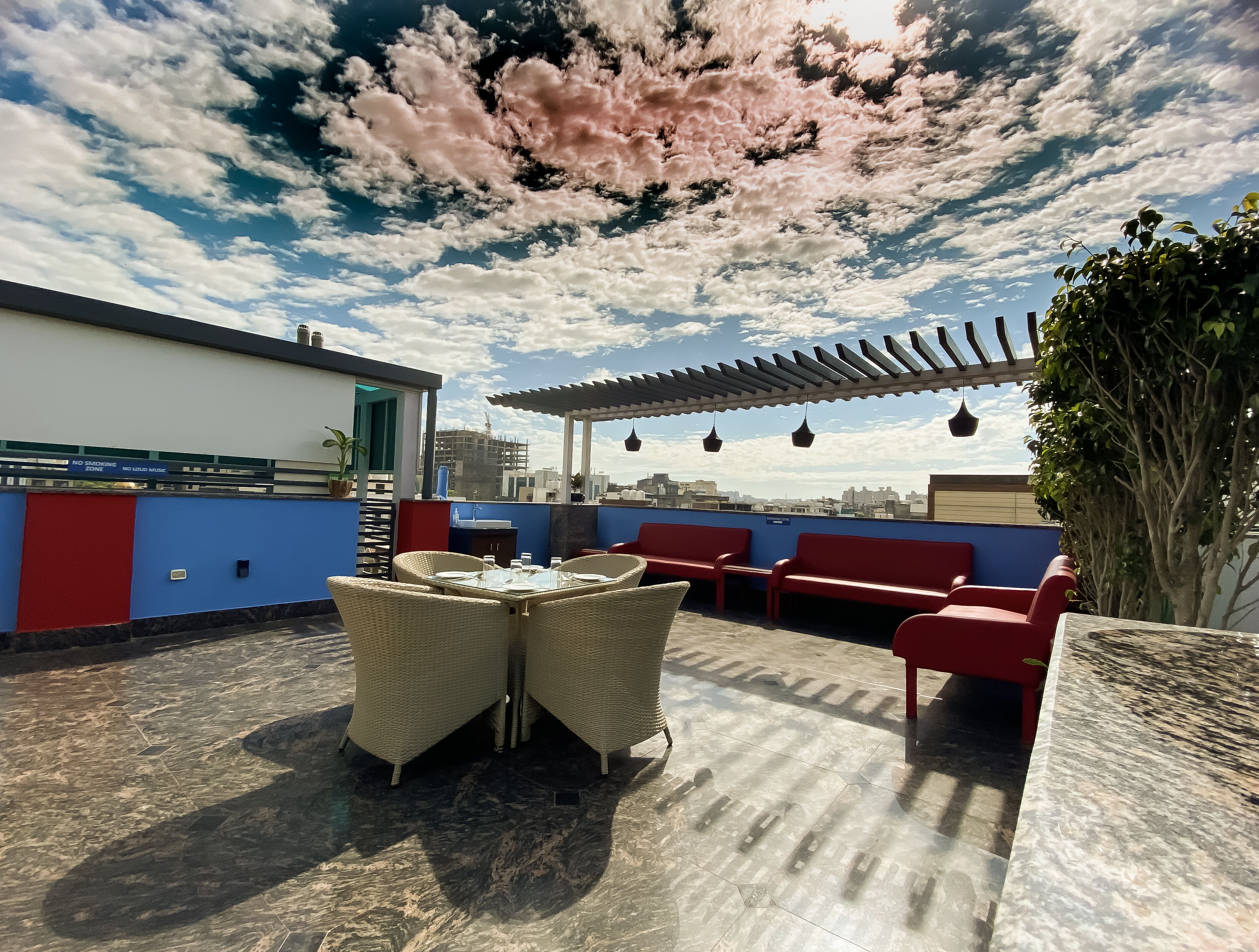 A rooftop terrace with a pergola, red seating, and a table with chairs.