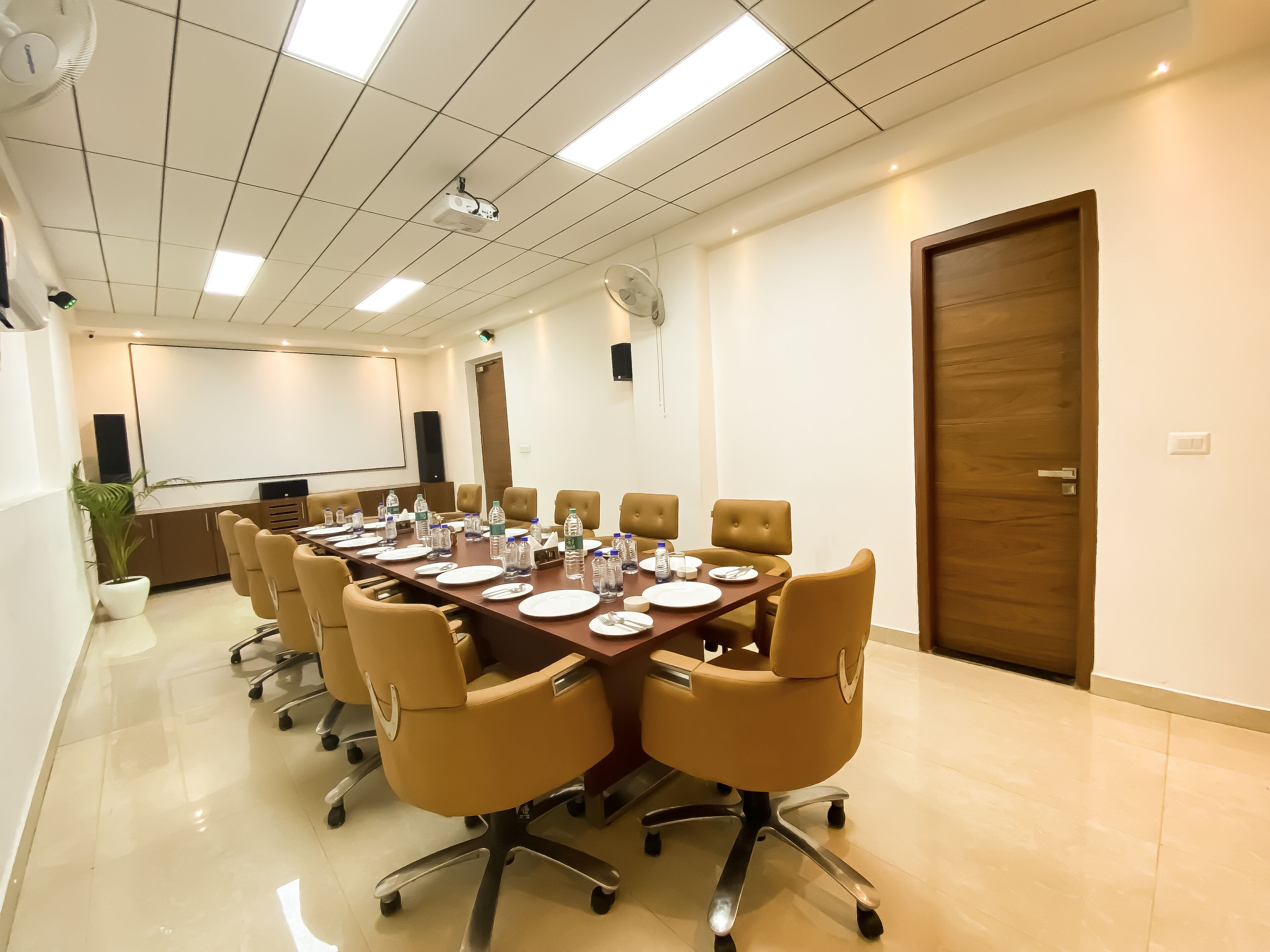 A conference room with a long table, multiple chairs, water bottles, and a projector screen.