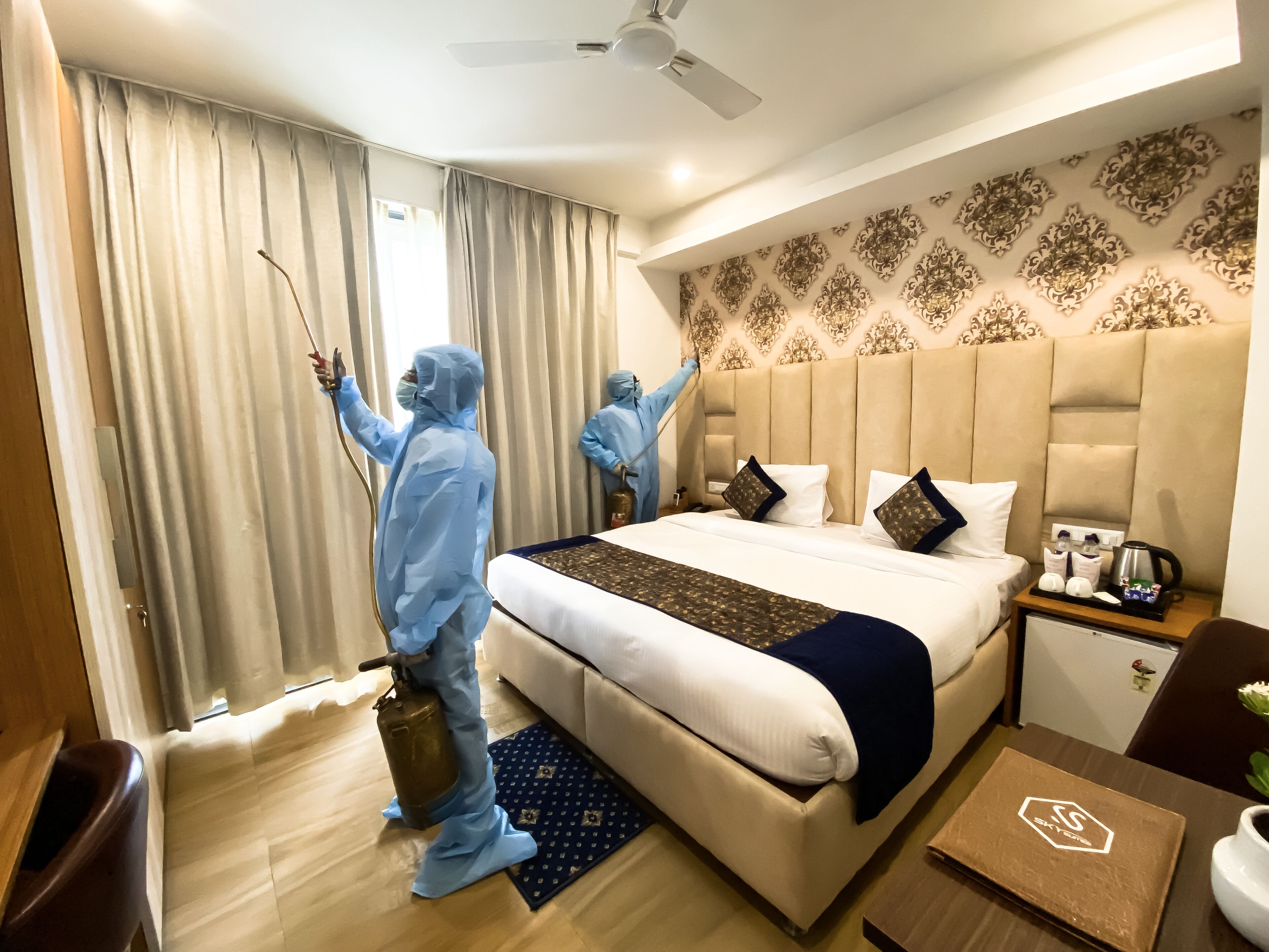 A hotel room with a large bed, a bedside table with a coffee maker, and a nightstand with a lamp.