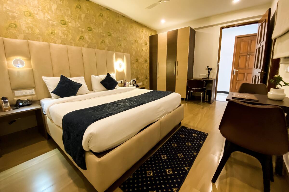 A hotel room with a bed, bedside tables, a desk, a chair, a desk lamp, a plant, and a ceiling fan.