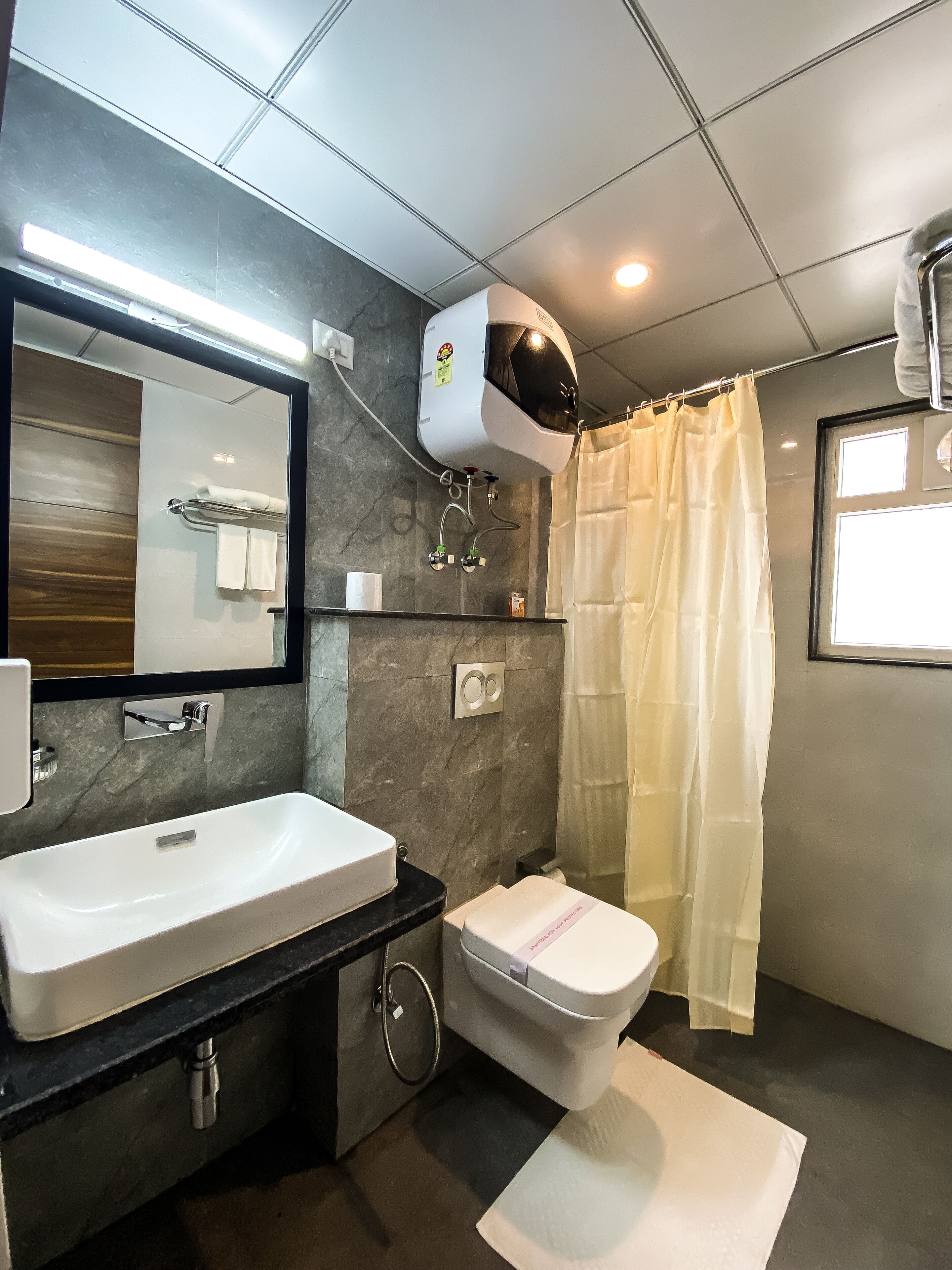 Een moderne badkamer met een groot wastafel, toilet, douchegordijn en spiegel.