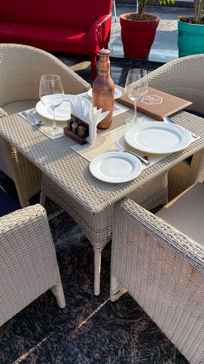 Un ensemble de mobilier de jardin en osier comprenant une table, des assiettes, des verres et une bouteille, entouré de chaises en osier et d’un canapé rouge.