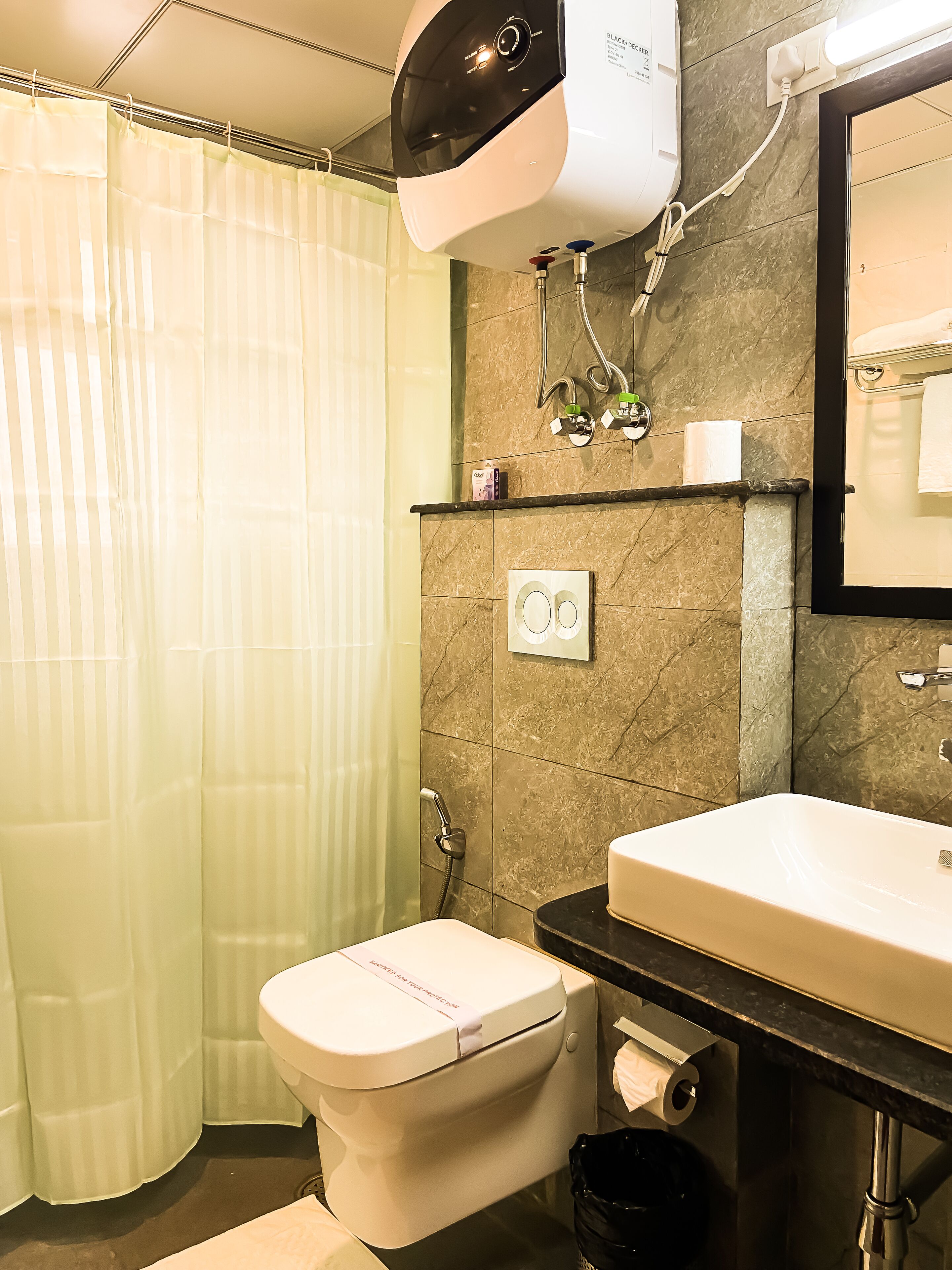 Ein Badezimmer mit Toilette, Waschbecken, Spiegel, Duschvorhang und Handtuchhalter.
