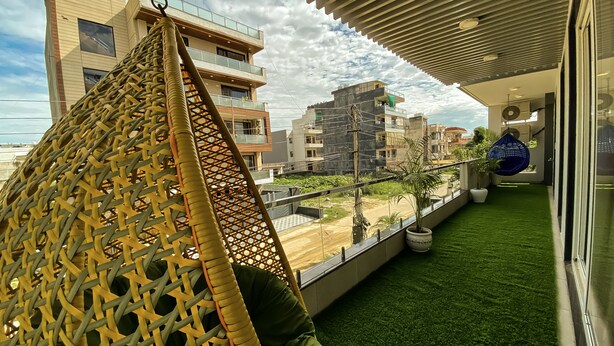 A balcony with artificial grass, a hanging chair, and a view of surrounding buildings. - Sky Suites Huda City Center (Gurugram)