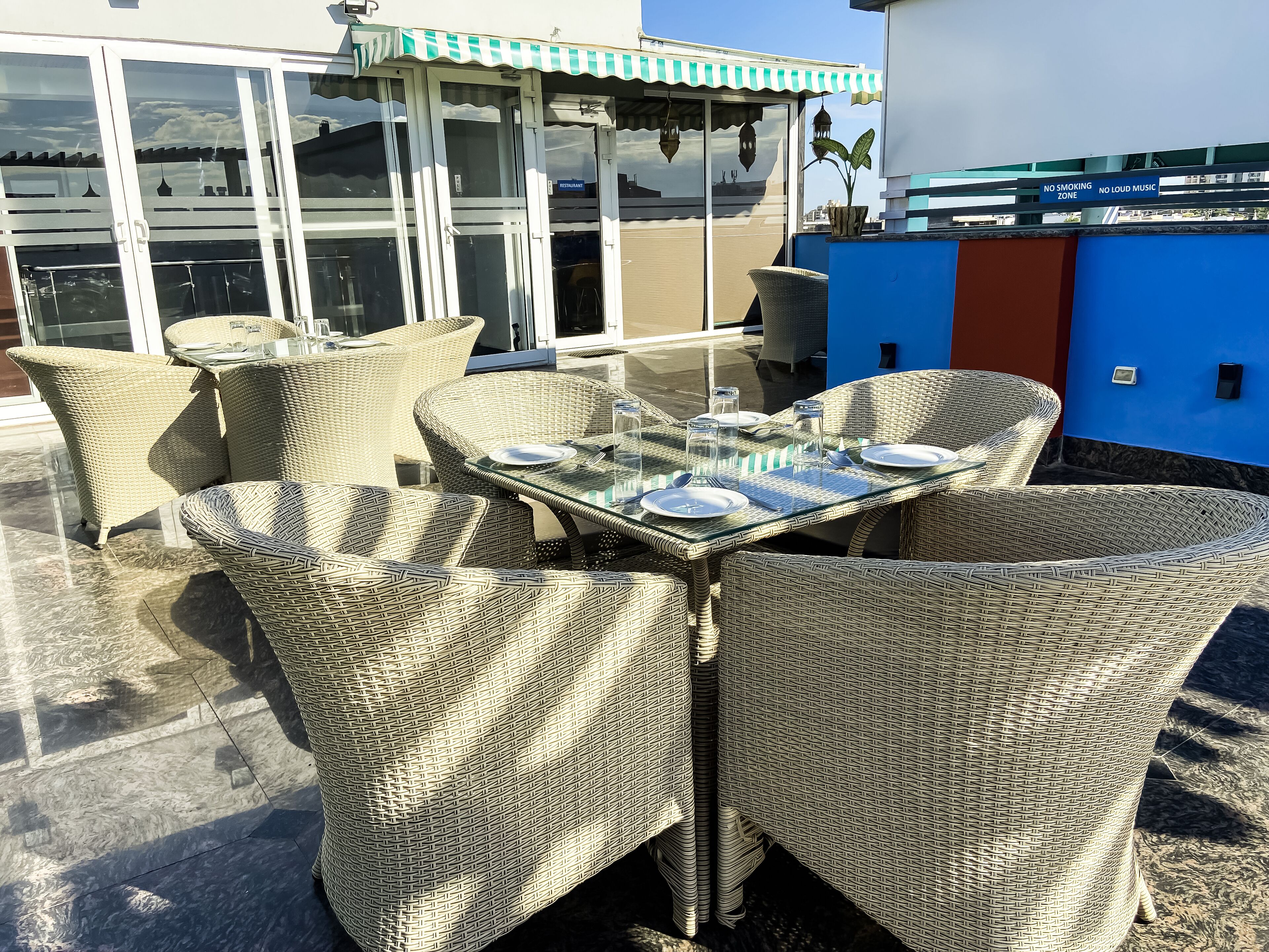 A rooftop terrace with wicker furniture and a glass table set for dining.