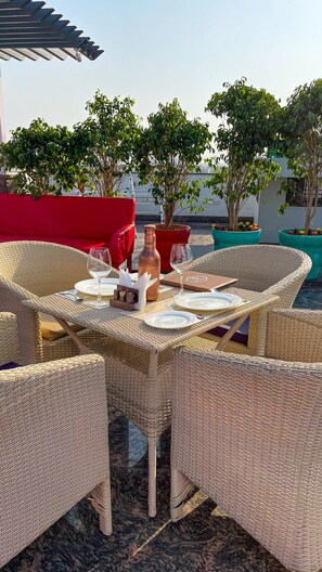 Un área de comedor al aire libre con mobiliario de mimbre, un sofá rojo y plantas en macetas.