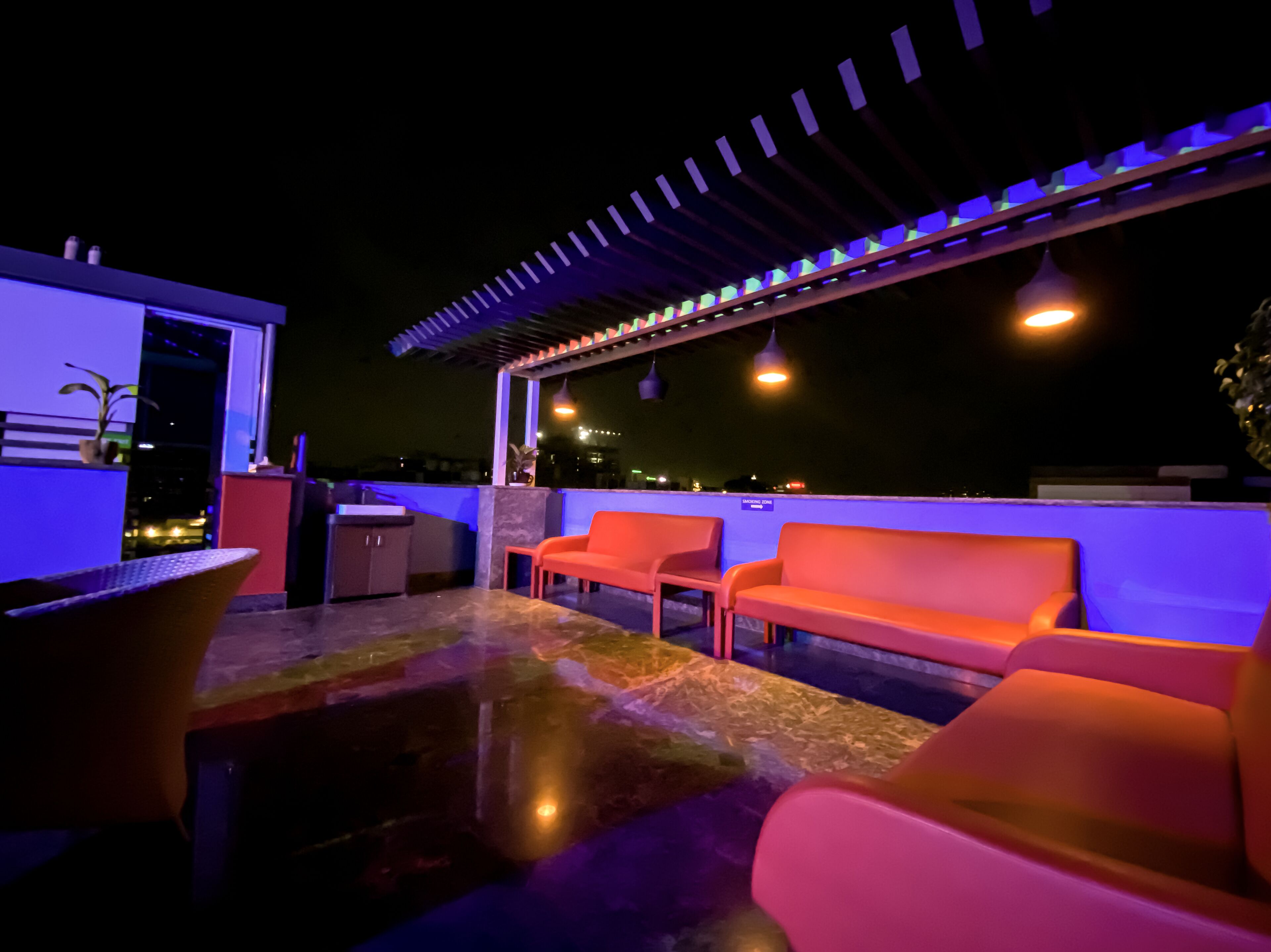 Una terraza en la azotea con una cocina exterior moderna, zona de estar y vistas a la ciudad de noche.