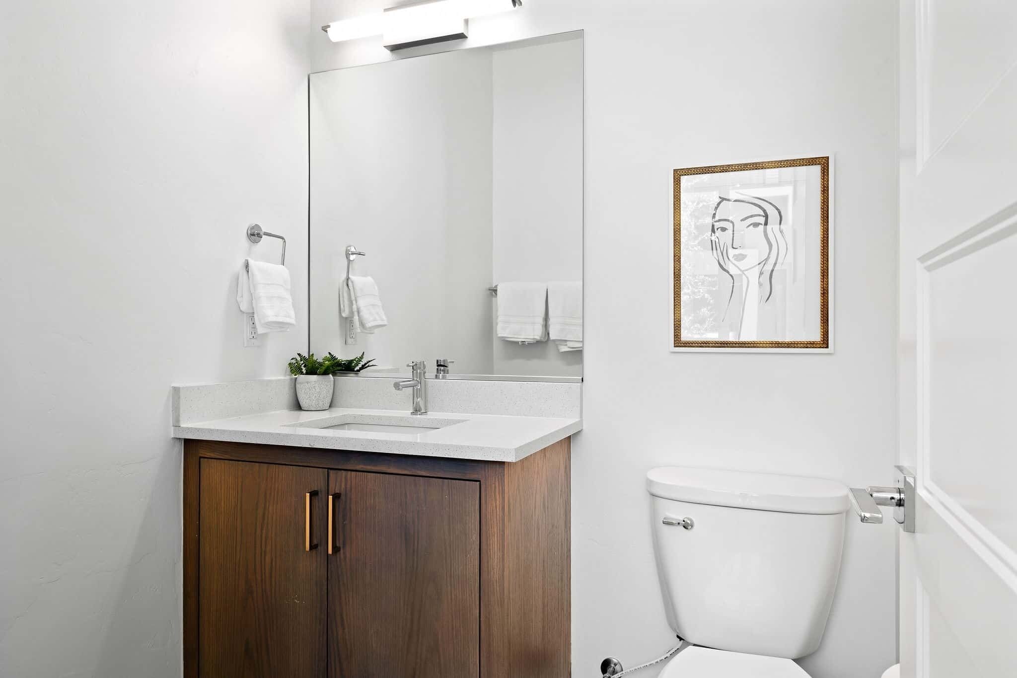Une salle de bain moderne avec un meuble-lavabo blanc, un grand miroir, une œuvre d’art encadrée et des toilettes.
