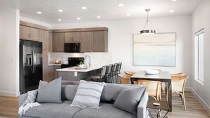 A modern kitchen with built-in appliances, a dining area with a table and chairs, and a living room with a sofa. - Family Paradise at the Vue by RedAwning (St. George)