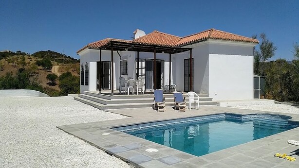 A modern house with a swimming pool, a covered patio, and a view of the surrounding landscape.