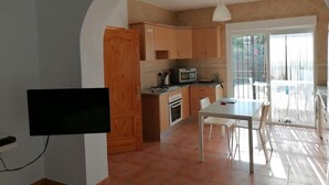A compact kitchen with wooden cabinets, a microwave, and a gas stove. There's a dining table with chairs and a TV mounted on the wall.