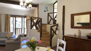 A dining area with a table set for breakfast, a staircase, and a living room with a sofa and curtains.