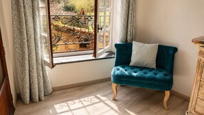 Quarto com janela, uma poltrona estofada em tons de verde-água e um armário de madeira.