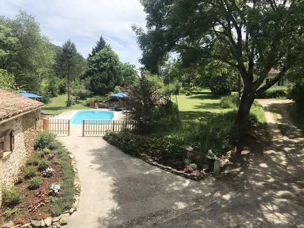 A backyard with a swimming pool, surrounded by a wooden fence, and a garden with various plants and flowers.
