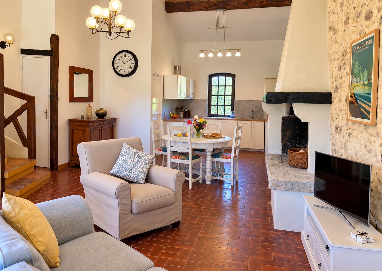 Ein Wohnzimmer mit einer Couch, einem Esstisch mit Stühlen, einer Küchenzeile, einem Kamin und einem Fernseher.