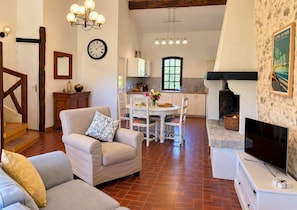 Uma sala de estar com sofá, mesa de jantar com cadeiras, área de cozinha, lareira e televisão.