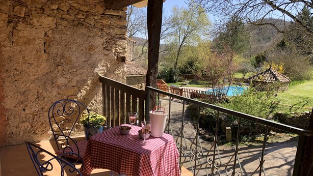 A balcony with a checkered tablecloth, two metal chairs, and a potted plant.