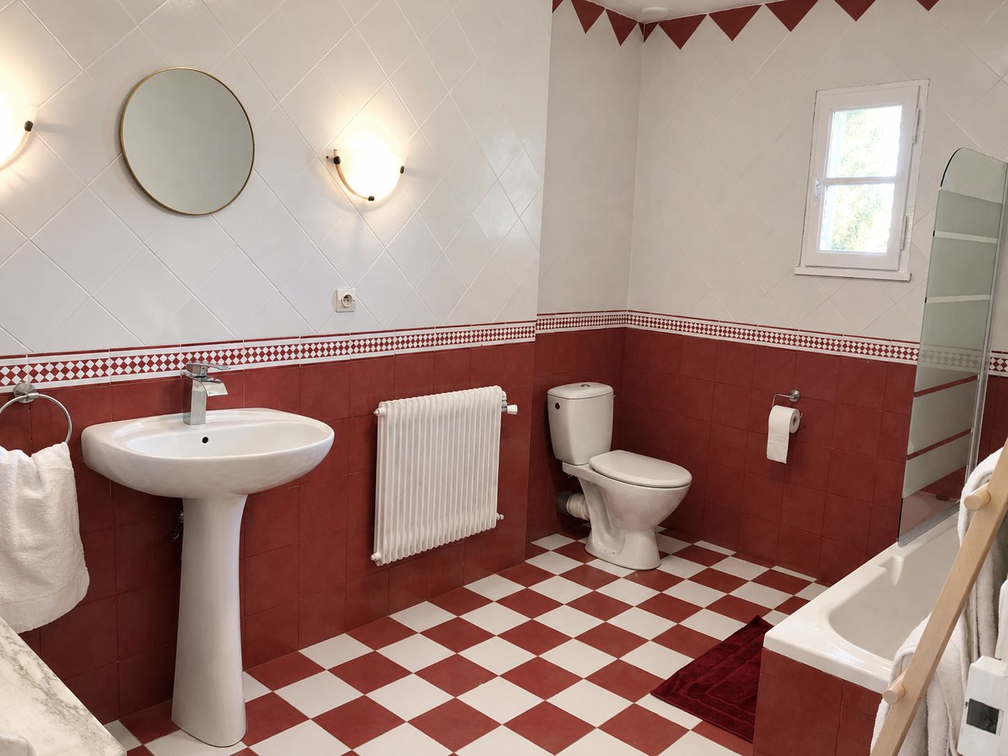 A bathroom with a white sink, toilet, and bathtub, red and white checkered floor, and a mirror on the wall.