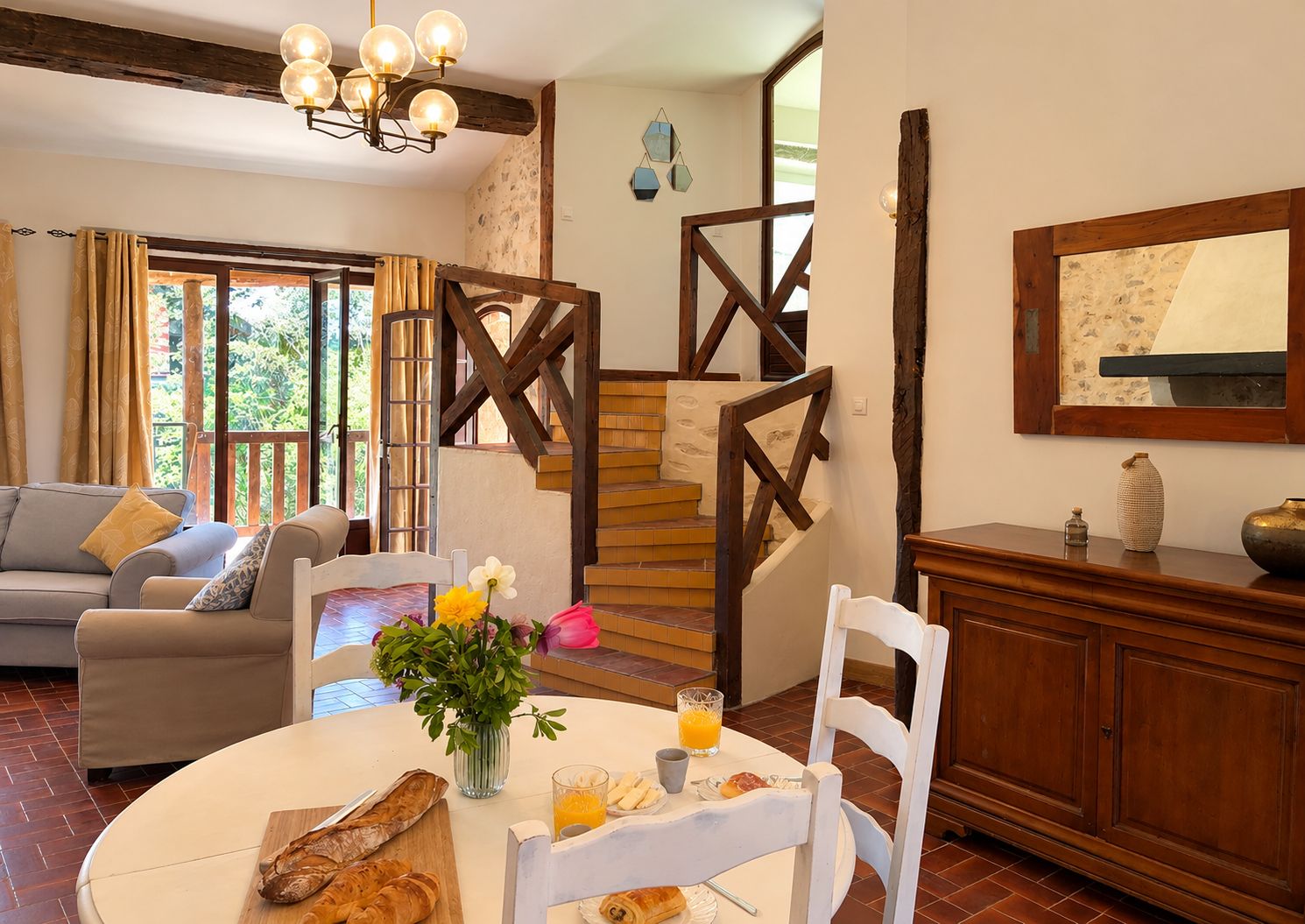 A dining area with a round table, chairs, a vase with flowers, and a breakfast setting including bread and juice.
