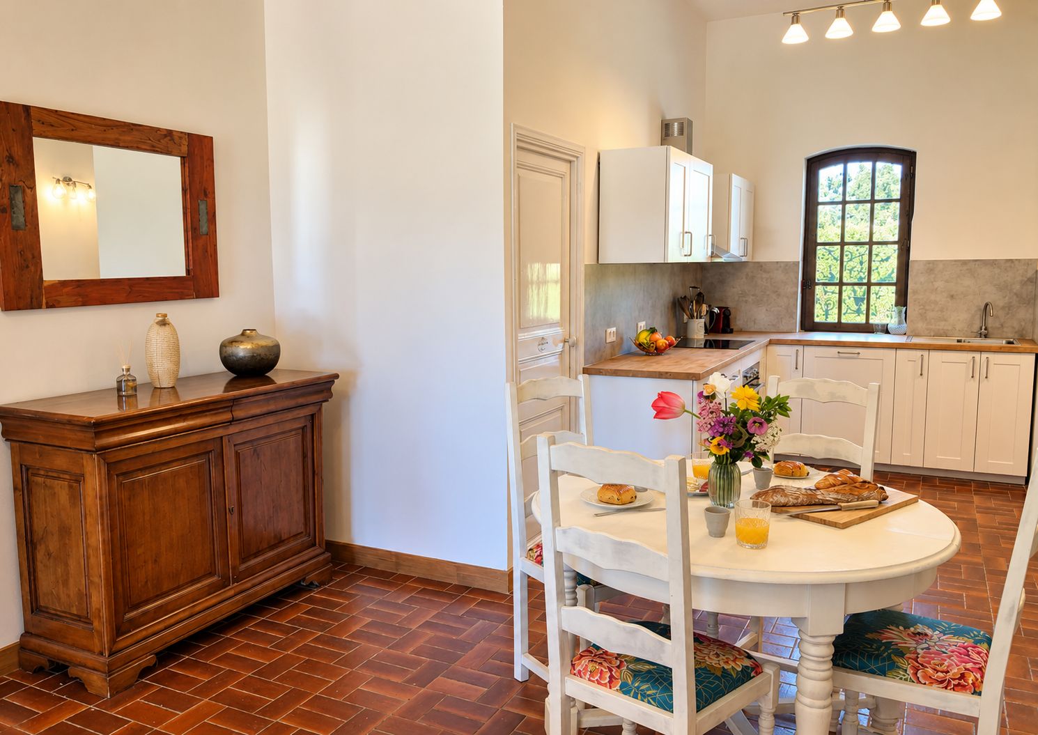 A kitchen with white cabinets, a wooden dining table with chairs, and a window with a view.