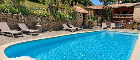 A clear blue swimming pool with lounge chairs and a stone wall.