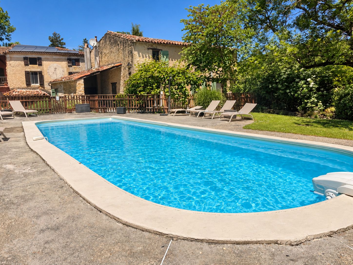 A rectangular swimming pool with clear blue water, surrounded by a concrete deck. There are lounge chairs along the poolside.