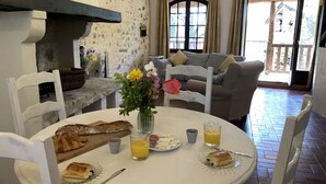 A dining area with a round table set for breakfast, featuring bread, pastries, and a glass of orange juice.
