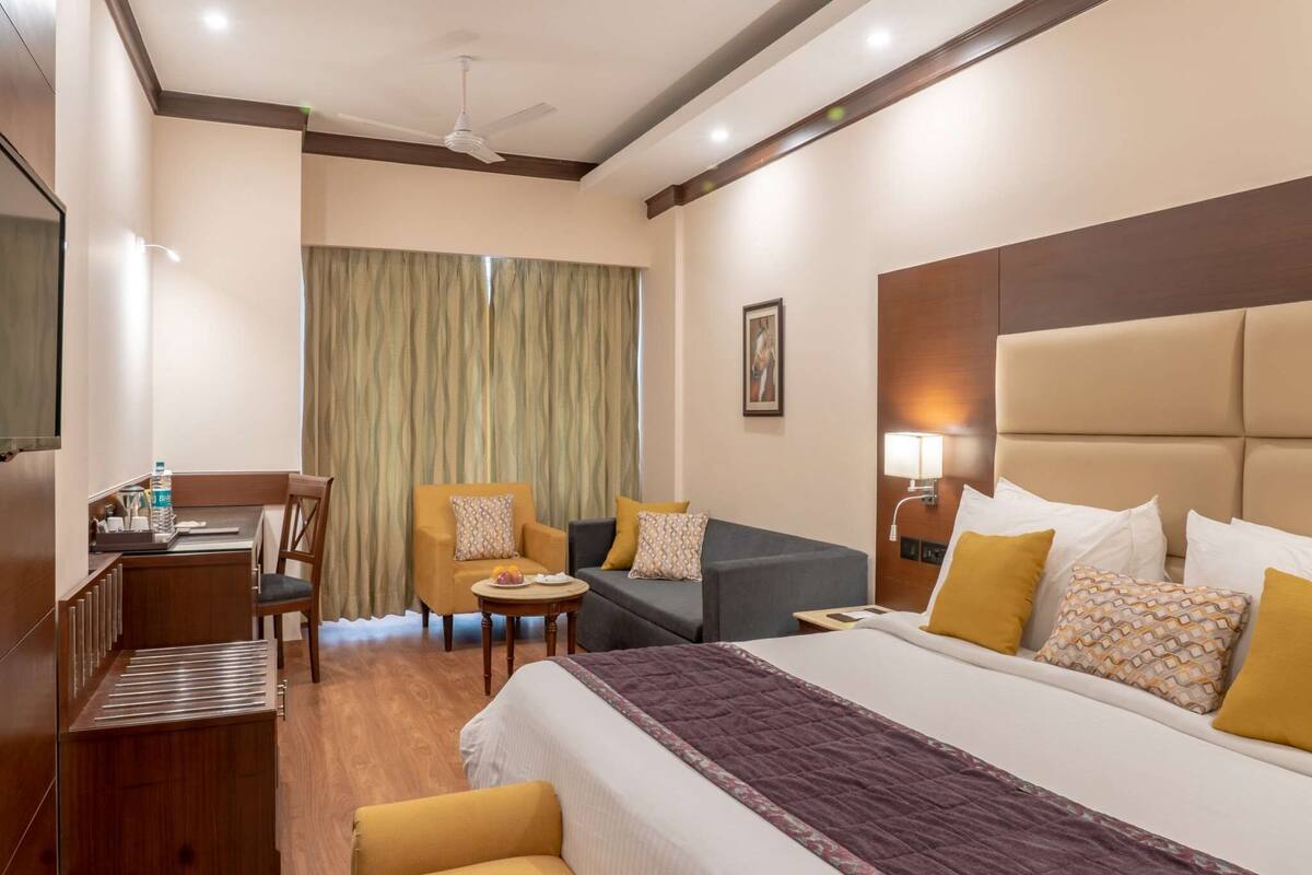 A hotel room with a bed, two armchairs, a sofa, a desk, and a chair.