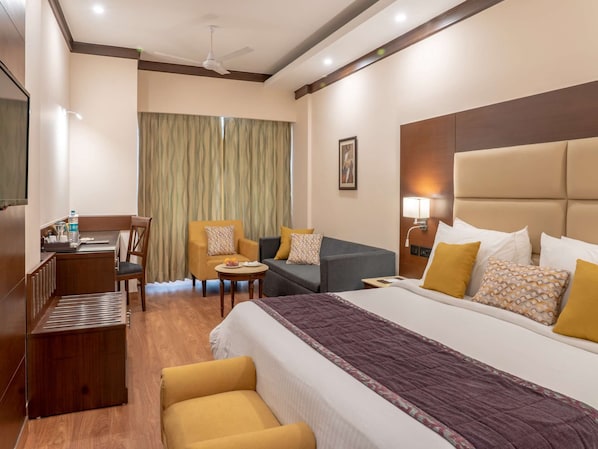 A hotel room with a bed, two armchairs, a sofa, a desk, and a chair.