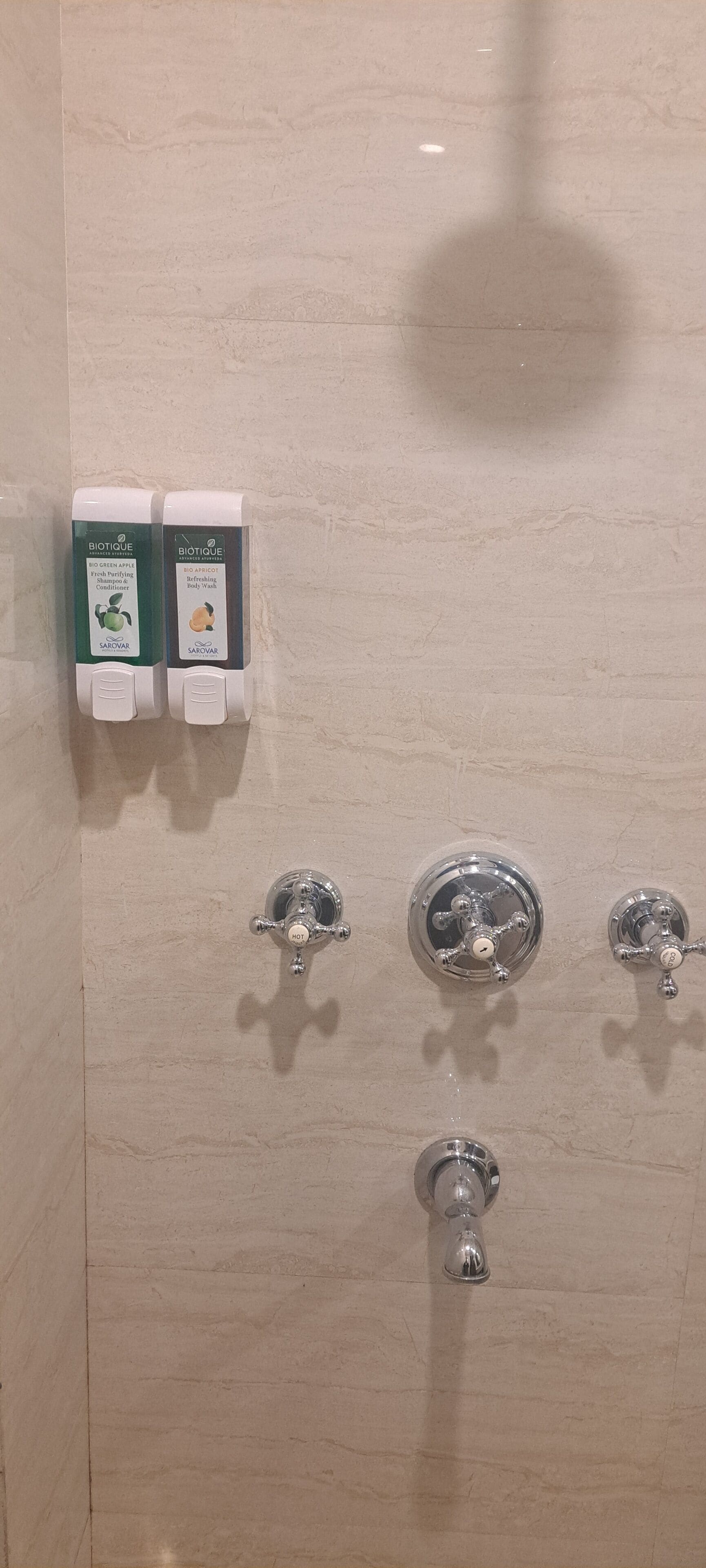 A bathroom with two hand soap dispensers, three faucets, and a showerhead.