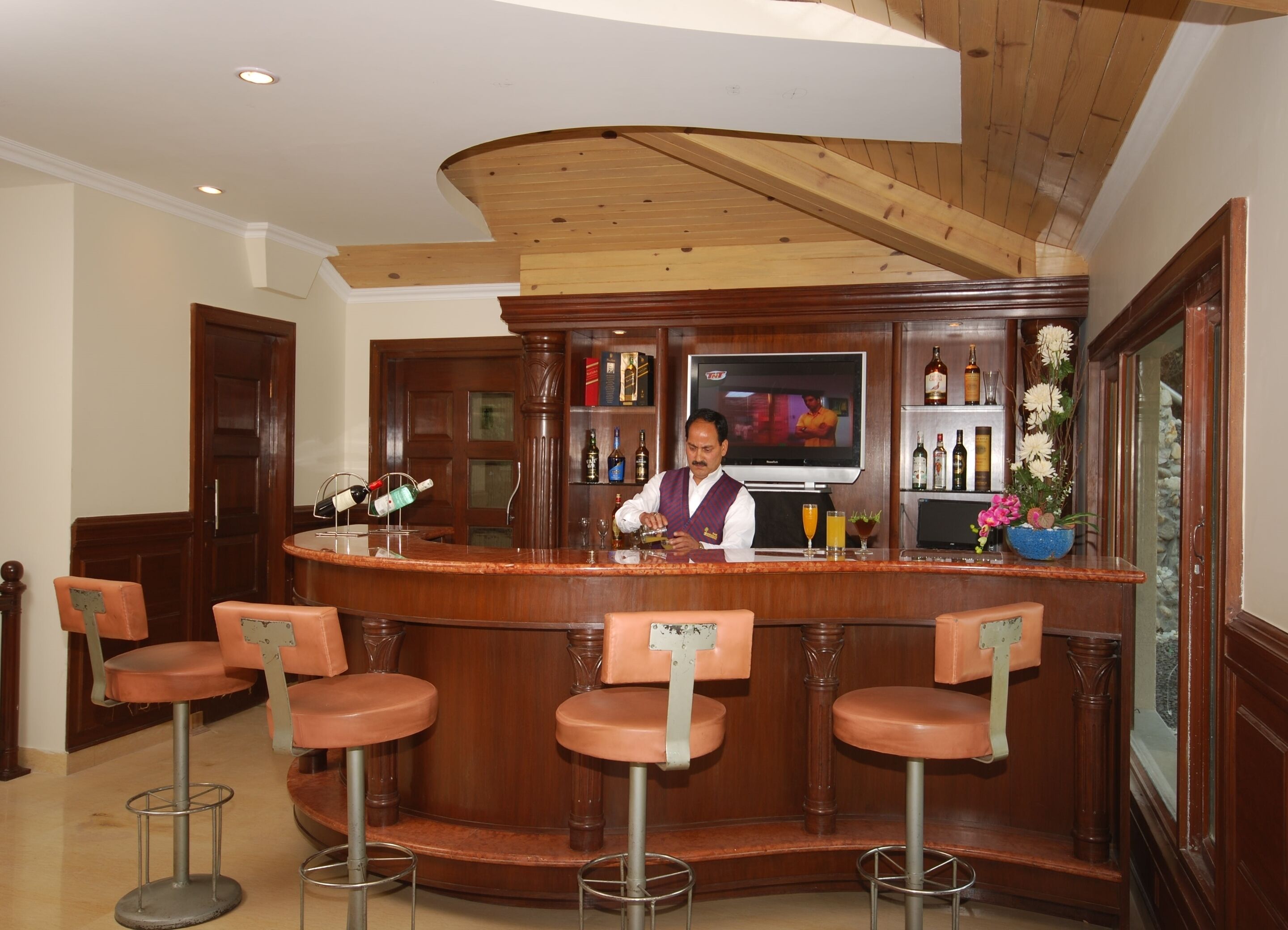 Zona de bar con un cantinero, mostrador de madera y cuatro taburetes.