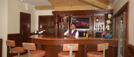 Zona de bar con un cantinero, mostrador de madera y cuatro taburetes.