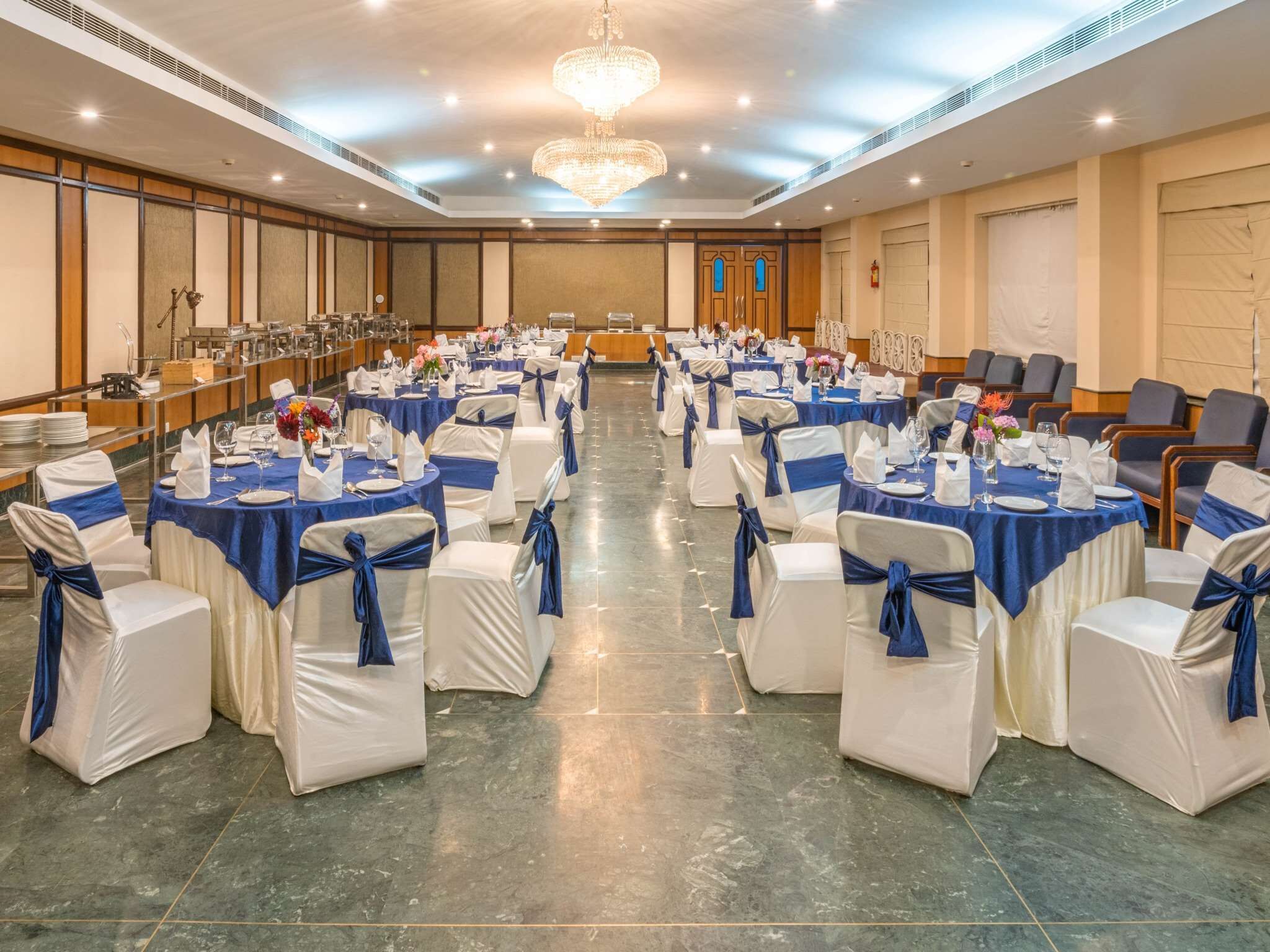 A banquet hall with round tables, white chairs, and blue sashes.