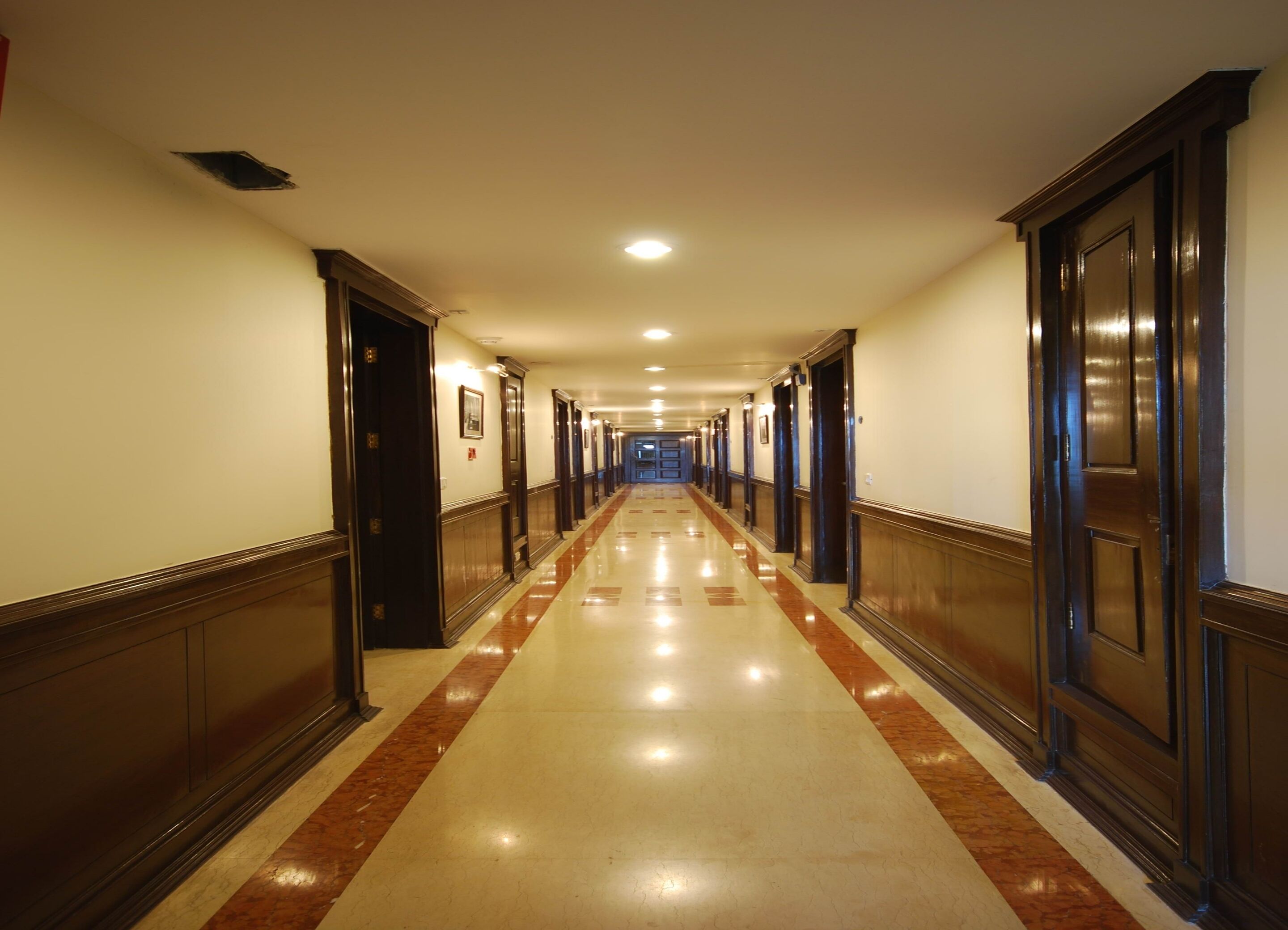 A long, well-lit hallway with wooden doors and a polished floor.