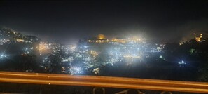 A nighttime cityscape with illuminated buildings and a prominent hilltop structure.