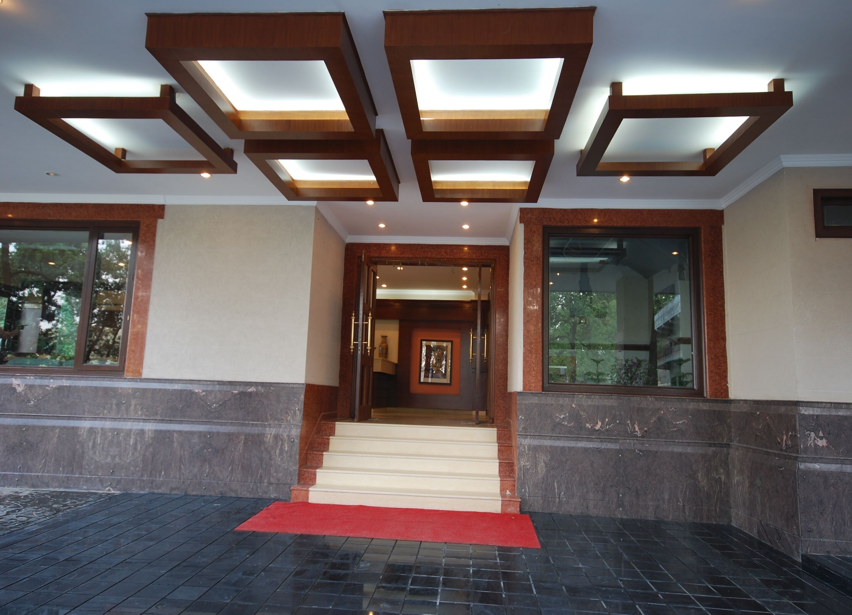 Entrada de hotel con alfombra roja, una escalera y un diseño moderno en el techo.