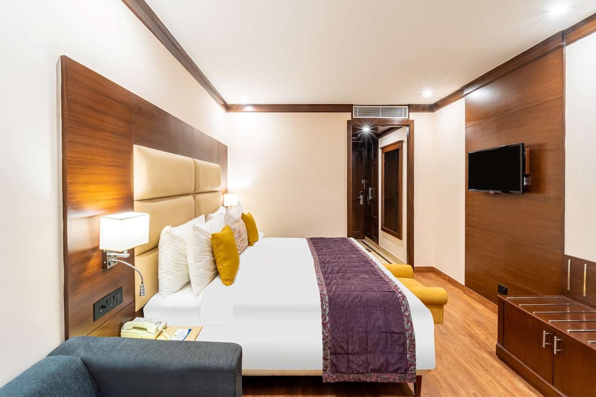 A hotel room with a large bed, bedside tables, a TV, and a wardrobe.