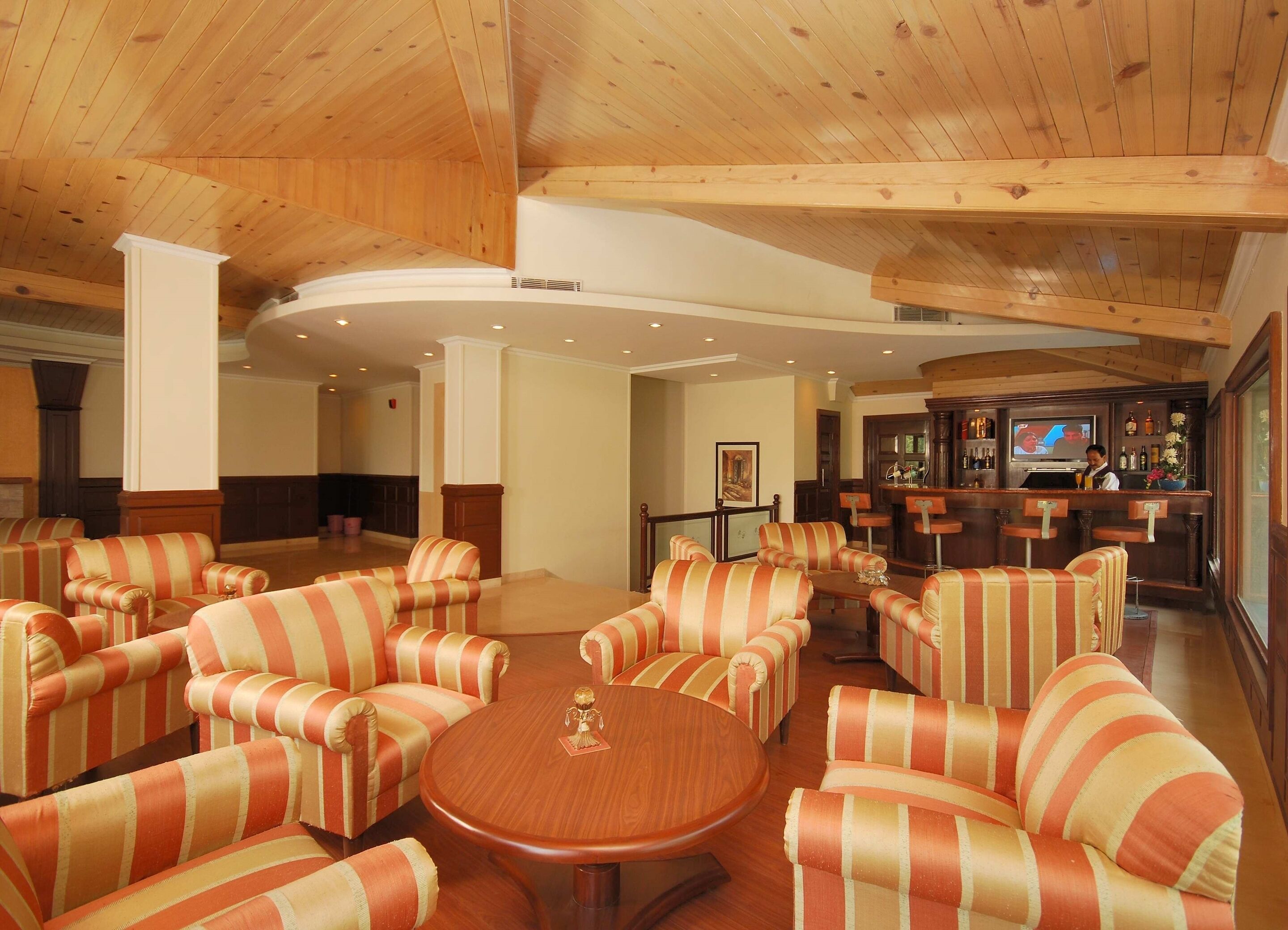 A spacious lobby with striped sofas, a round wooden table, and a bar area with a television.