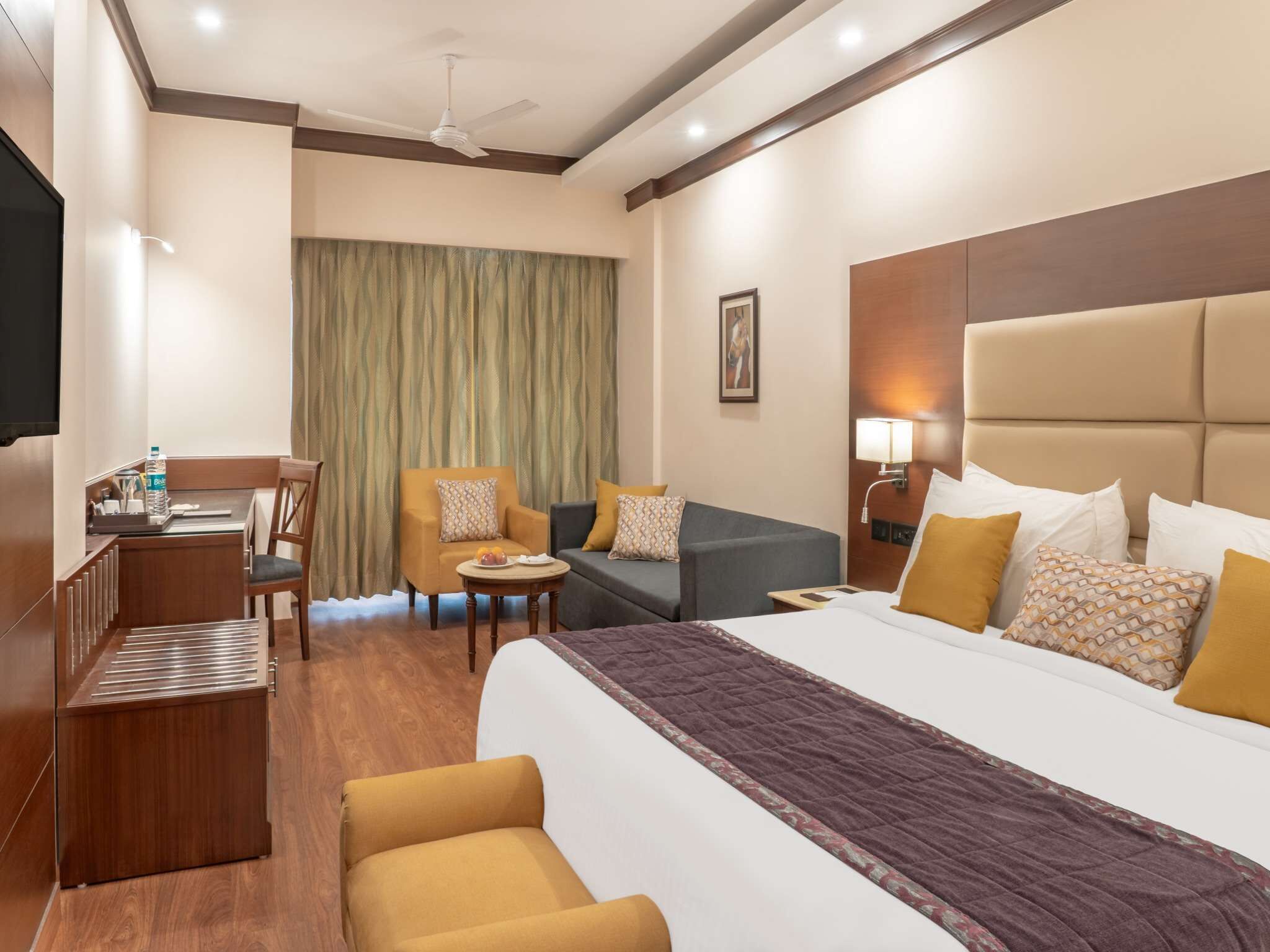 A hotel room with a bed, a desk, a chair, a sofa, and a small table.