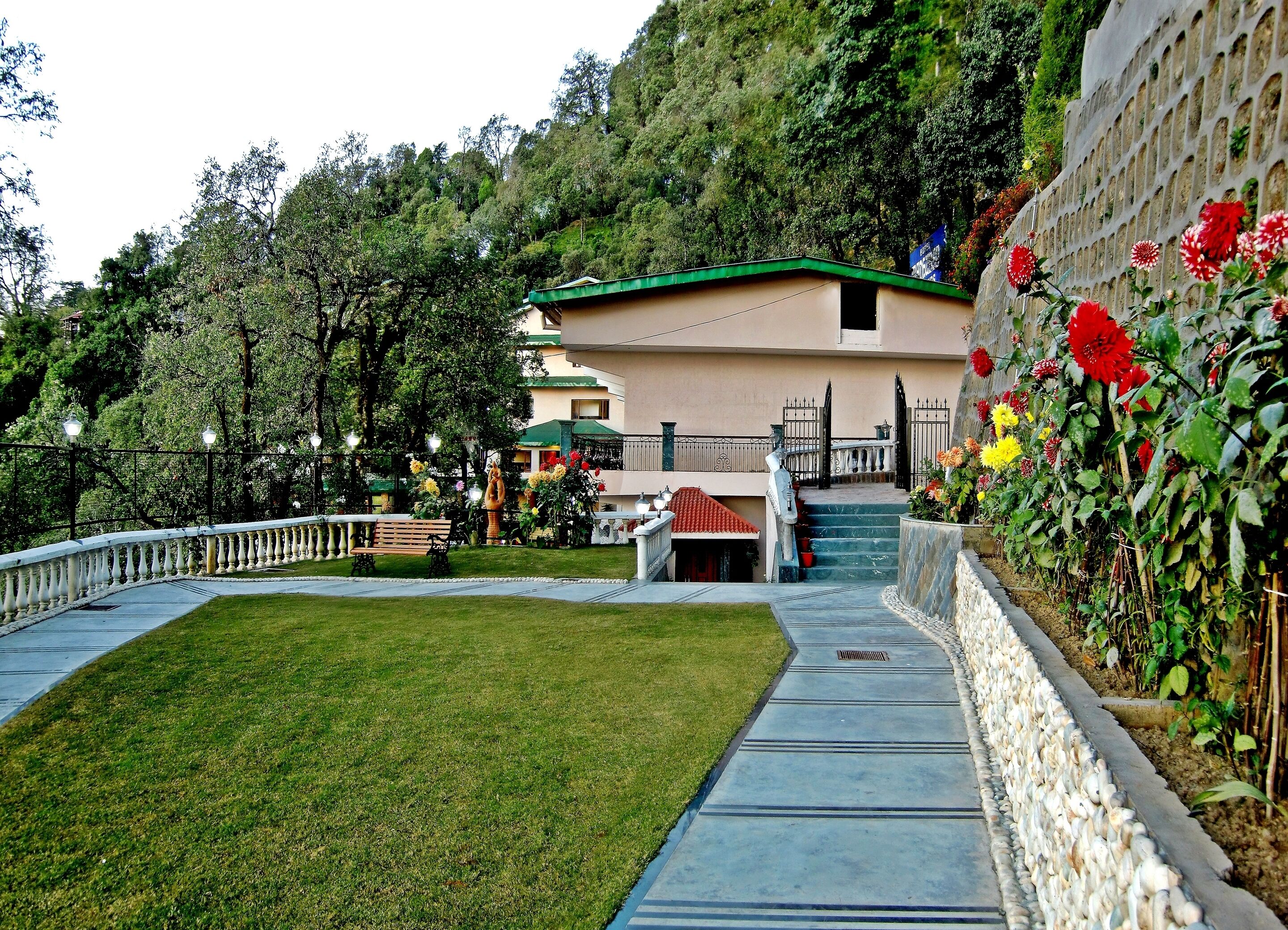 Ein Hotel mit einem grasgedeckten Gebäude, einer Rasenfläche, einem gepflasterten Weg und einem Blumengarten mit roten und gelben Blüten.