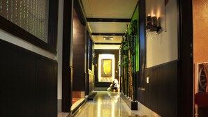A hallway with a polished marble floor, a reception desk, a Buddha statue, and a wall-mounted light fixture.